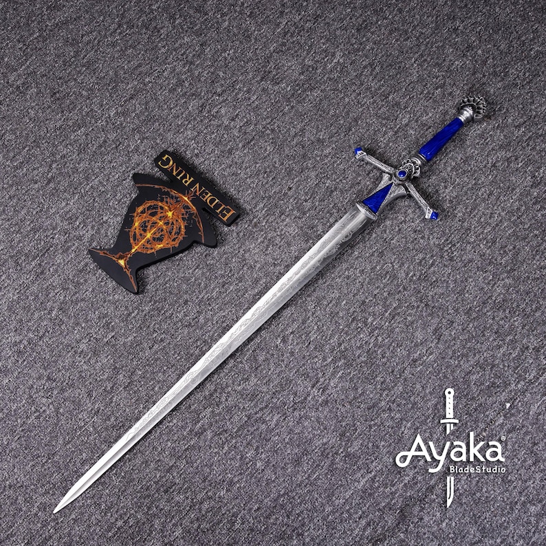 May include: A silver sword with a blue handle and crossguard, featuring intricate detailing. The sword is displayed with a black Elden Ring emblem. The Ayaka Blades Studio logo is visible in the bottom right corner.