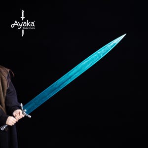 May include: A long, blue sword with a textured blade and ornate silver hilt. The blade has a unique pattern and a sharp point. The sword is held against a black background. The logo "Ayaka BladeStudio" is in the upper left corner.