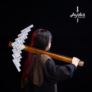 Op de afbeelding: Een houten zeis met een gepixelde kling wordt over de schouder van een persoon gehouden. De zeis heeft een bruine steel en een grijze kling. De achtergrond is zwart en het logo "Ayaka BladeStudio" is zichtbaar.