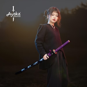 Puede incluir: Una katana con empuñadura morada y hoja negra con diseño azul y blanco. La espada se sostiene frente a una persona. El logotipo "Ayaka BladeStudio" está en la esquina superior izquierda.