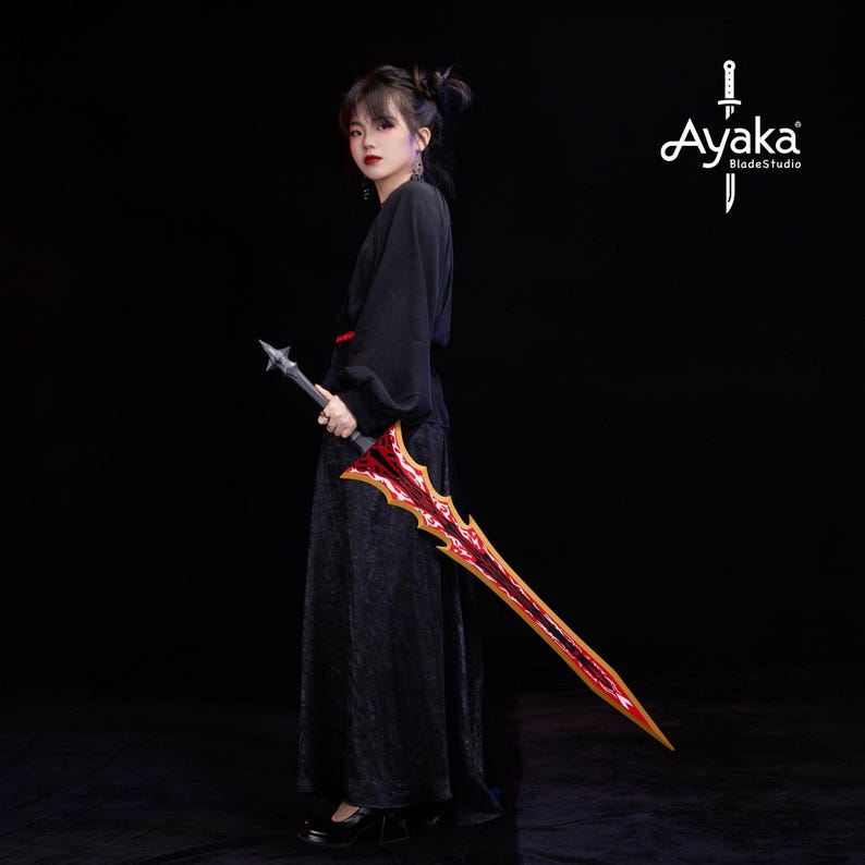 May include: A long, ornate sword with a red and gold blade is held by a person in a black outfit. The sword has a detailed design and a spiked handle. The logo "Ayaka BladeStudio" is visible in the upper right corner.