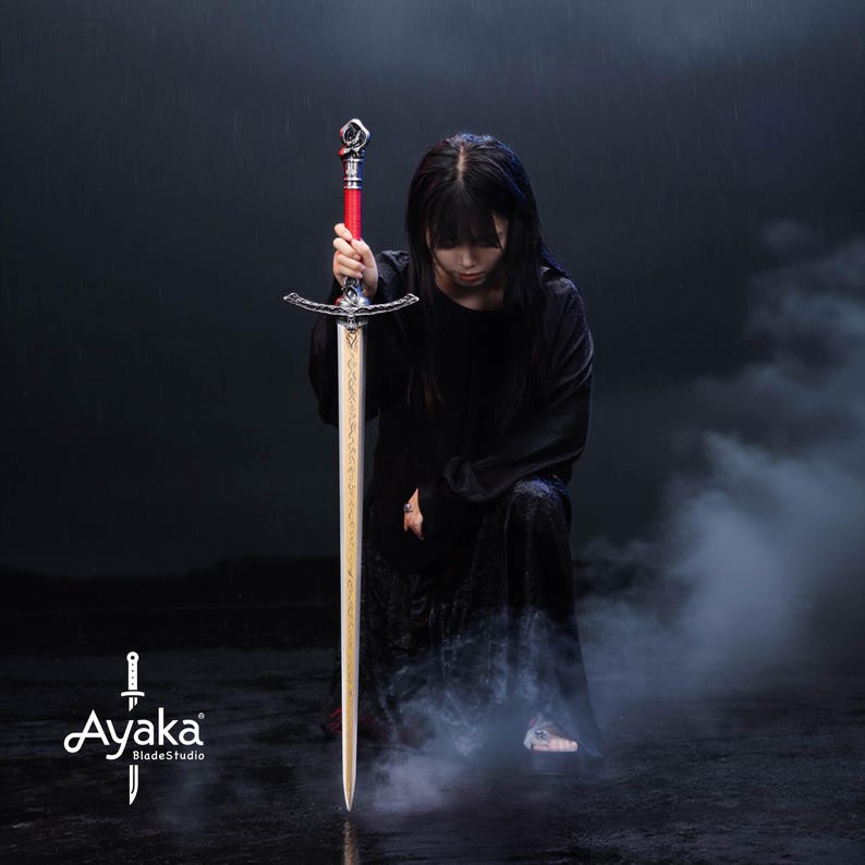 May include: A long sword with a silver crossguard and a red handle. The blade is gold with etched designs. The sword is held by a person in a black dress. The image has the text "Ayaka BladeStudio".