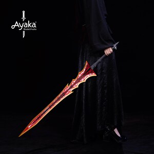May include: A decorative sword with a red and gold blade and a black handle. The blade has a unique, jagged design. The sword is held by a person wearing a black outfit. The Ayaka BladeStudio logo is in the upper left corner.