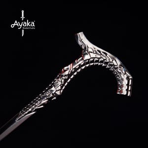 May include: A silver-colored walking cane with a detailed, textured design. The handle and shaft feature an intricate pattern, and the cane is set against a black background. The logo "Ayaka BladeStudio" is visible in the upper left corner.