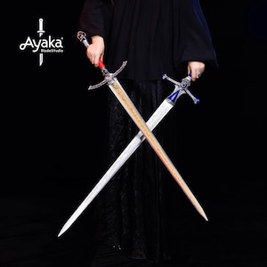 May include: Two crossed swords with ornate silver hilts and blades. One sword has a red handle and gold accents, the other has a blue handle. The blades are etched with designs. The Ayaka BladeStudio logo is in the upper left corner.