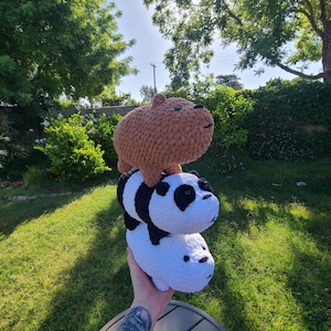 May include: Three plush animal toys stacked on top of each other. The top toy is a brown capybara, the middle is a panda bear with black and white markings, and the bottom is a white polar bear.