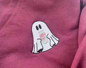 May include: Burgundy sweatshirt with a white ghost patch. The ghost has black eyes and a design on its body that says "Poppy Diet". The sweatshirt is made of a soft material.