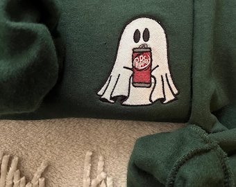May include: Dark green sweatshirt with an embroidered ghost holding a Dr. Pepper can. The ghost is white with black eyes and a black outline. The Dr. Pepper can is red with white lettering.