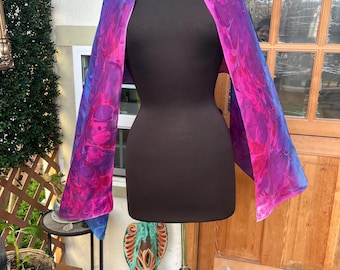 May include: A vibrant, abstract-patterned scarf in shades of blue, pink, and purple is draped over a black mannequin. The scarf's design features a flowing, marbled effect, creating a unique and artistic accessory.