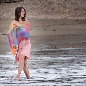 May include: A woman wearing a pink dress and a colorful shawl walks through the shallow water of a beach.