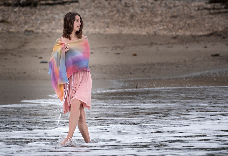 May include: A woman wearing a pink dress and a colorful shawl walks through the shallow water of a beach.