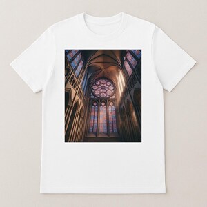 May include: White t-shirt featuring a detailed image of a cathedral interior. The image showcases stained glass windows, arched ceilings, and columns, with sunlight streaming through the windows. The design captures the architectural beauty of the building.