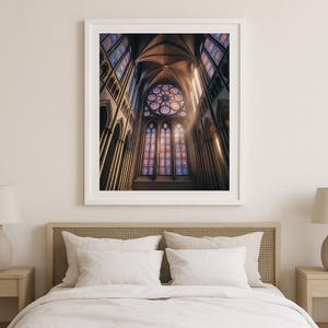 May include: A framed print of a cathedral interior, showcasing stained glass windows and architectural details. The image captures the upward perspective of the building, with sunlight streaming through the windows. The color palette includes shades of brown, red, blue, and gold.