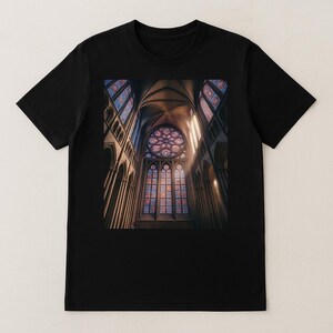 May include: Black t-shirt featuring a detailed image of a cathedral interior. The image showcases stained glass windows in shades of blue, red, and purple, with sunlight streaming through. The architectural details include arched ceilings and columns.