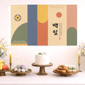 May include: A festive table setting with a banner featuring Korean text and abstract shapes. The table displays a white cake, fruits, pastries, and pastel-colored eggs. Vases of flowers and lit candles flank the scene, creating a celebratory atmosphere.