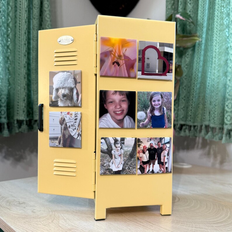 May include: A yellow miniature locker with a black handle and several square magnets attached. The magnets display various photographs, including images of a dog, children, and flowers. The locker is on a light-colored wooden surface.