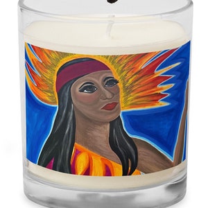 May include: A clear glass candle with a painted image of a woman with a red headband and a colorful headdress. A lit match is held above the candle, ready to light the wick. The candle has a white wax.