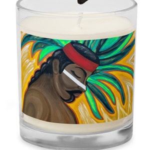 May include: A clear glass candle jar with a white candle inside. The jar has a colorful label with a painting of a person with a headdress and a green and yellow background.