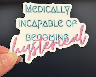May include: A white sticker with the text "MEDICALLY INCAPABLE OF BECOMING hysterical" in teal and pink lettering. The sticker has a unique shape and is held by a person's fingers against a dark background.