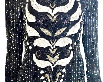 Puede incluir: Top negro de manga larga con diseños florales y abstractos de lentejuelas blancas y plateadas. El top presenta un cuello redondo y está cubierto de pequeñas cuentas blancas. Las mangas tienen filas verticales de cuentas blancas.