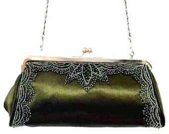 May include: An olive green satin clutch with a silver chain strap. The clutch features intricate beadwork along the top and sides, creating a decorative border. The clasp is silver-toned, adding to the bag's elegant design.