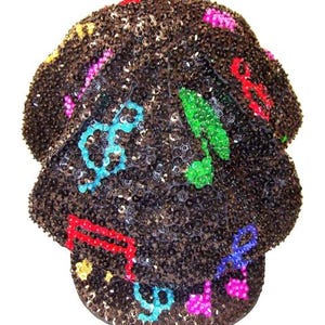 May include: A black sequined baseball cap adorned with colorful musical notes in red, green, blue, and pink. The cap is covered in small, shiny sequins, creating a textured surface. The brim is curved and the cap has a classic six-panel design.
