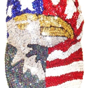 Puede incluir: Una gorra de béisbol totalmente cubierta de lentejuelas con un diseño patriótico. La parte delantera muestra una cabeza de águila calva en oro y blanco, sobre un fondo de rayas rojas, blancas y azules y un campo azul con estrellas blancas.
