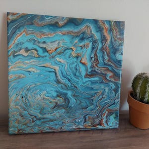 May include: Abstract acrylic painting on canvas with a fluid art design. The artwork features swirling patterns in shades of turquoise, brown, and gold. The painting is displayed next to a small potted cactus in a terracotta pot.
