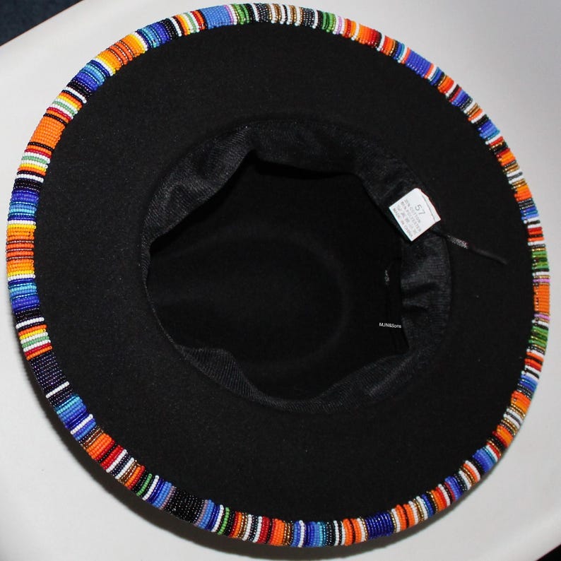 May include: Black fedora hat with a colorful beaded band around the brim. The band features a pattern of blue, orange, green, and white beads. The hat has a black interior and a tag with the number 57.