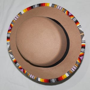 Puede incluir: Un sombrero fedora color canela con un ribete de cuentas. El ribete presenta un patr&oacute;n de cuentas rojas, naranjas, amarillas, blancas, grises y moradas. El sombrero tiene una banda interior negra y una corona redondeada.