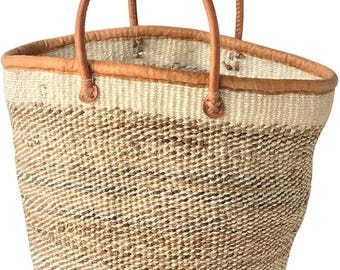 Puede incluir: Bolso de cesta tejido con asas y ribetes de cuero marrón. El bolso presenta una paleta de colores natural y neutra con un diseño tejido. Las asas están sujetas con detalles de cuero.