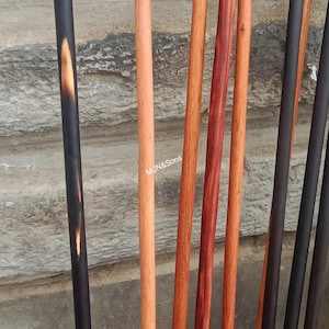 May include: A collection of wooden walking sticks and canes in various colors and finishes. The sticks range from light tan to dark brown and black, with a smooth, polished appearance. Some have a darker handle.
