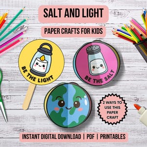 May include: An assortment of craft supplies, including colored pencils, scissors, and glue, arranged around three circular paper crafts. The paper crafts feature cute illustrations of a lantern, salt shaker, and globe, with the phrases "Be the Light" and "Be the Salt". The text "Salt and Light" and "Paper Crafts for Kids" are also visible.