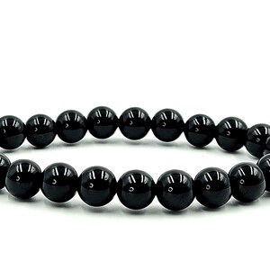 May include: A black beaded bracelet with glossy, round beads. The bracelet is made of multiple black beads strung together, creating a circular shape. The beads are evenly sized and spaced.