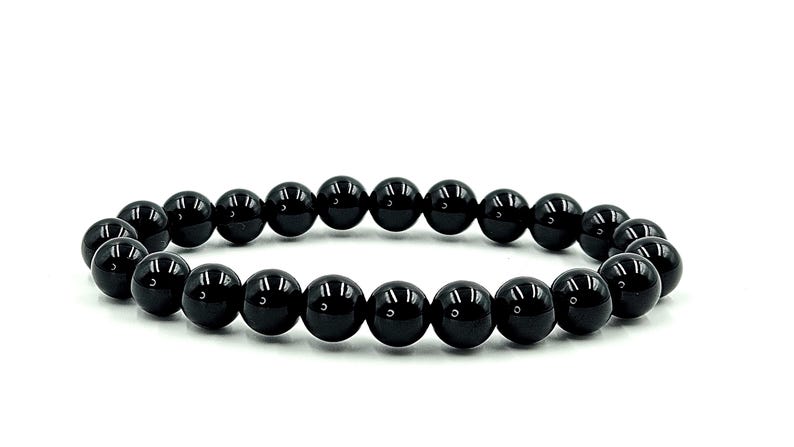 May include: A black beaded bracelet with glossy, round beads. The bracelet is made of multiple black beads strung together, creating a circular shape. The beads are evenly sized and spaced.