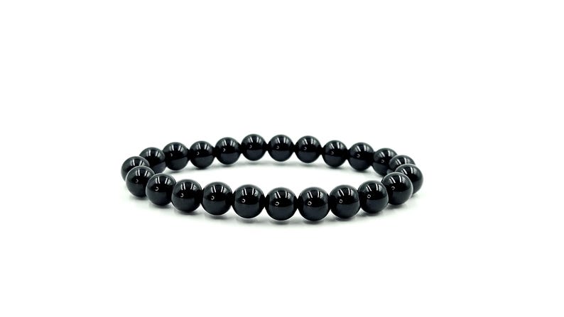 May include: A black beaded bracelet. The bracelet is made of polished, round, black beads strung together on an elastic band. The beads have a glossy finish and reflect light. The bracelet is displayed on a white background.