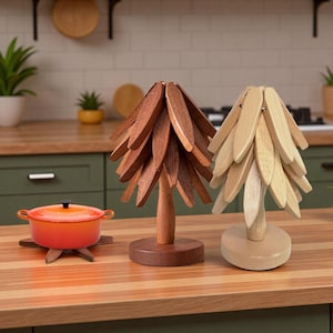 Könnte beinhalten: Zwei baumförmige Holzdekorationen und ein Topf. Ein Baum ist dunkelbraun, der andere hellbraun. Der orangefarbene Topf hat einen schwarzen Griff und steht auf einem hölzernen Untersetzer. Die Objekte stehen auf einer Holztheke.