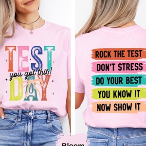 May include: A light pink t-shirt with the words "TEST DAY" in colorful block letters. The front of the shirt says "you got this!" and the back says "Rock the test, don't stress, do your best, you know it, now show it."