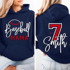 May include: Navy blue hoodie with the words "Baseball Mama" in white script and red lettering. The back of the hoodie features the number 7 in red with a white outline and the name "Smith" in white script.