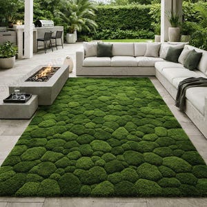 May include: A large, rectangular green rug with a textured, moss-like appearance. The rug is placed on a patio, near a white sectional sofa and a stone fire pit. The rug's dimensions are approximately 96 inches long and 60 inches wide.
