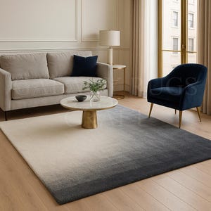 Pode incluir: Um tapete retangular grande com um design gradiente, que vai do bege claro ao cinza escuro. O tapete está em uma sala de estar, com um sofá, uma poltrona e uma mesa de centro. As dimensões do tapete são em centímetros.