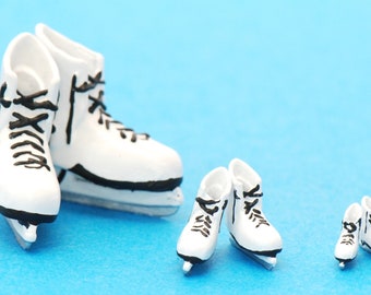 May include: Four pairs of white miniature ice skates with black laces. The skates are arranged in order of size, with the largest pair in the front and the smallest pair in the back.
