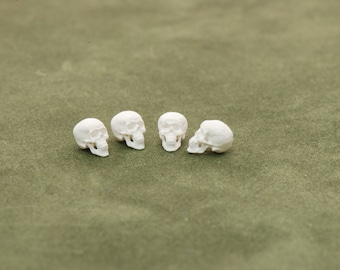 May include: Five small white ceramic skulls arranged in a row on a green surface.