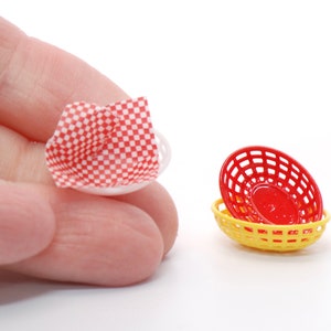 May include: Miniature red and yellow plastic food baskets and a small white dish with a red and white checkered paper liner. The baskets are oval-shaped with a lattice design. The dish is held by a hand.