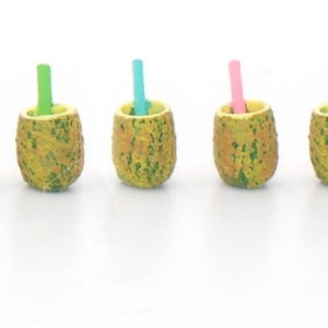 Puede incluir: Cinco tazas en miniatura con forma de piña con pajitas de colores. Las tazas son amarillas con detalles verdes y las pajitas son rosas, verdes y azules.
