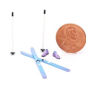 May include: A miniature set of blue skis, purple ski boots, and two white ski poles. The set is next to a US penny for scale.