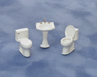 May include: White porcelain miniature bathroom set with a pedestal sink, toilet, and toilet seat.
