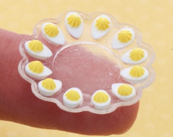 May include: A clear plastic serving tray with a scalloped edge holds 12 miniature deviled eggs. Each egg is topped with a yellow yolk and a white egg white.