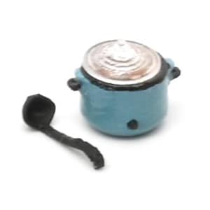 May include: A miniature blue cooking pot with a silver lid and black handles, next to a black ladle. The pot has a small black dot on the front. The items are likely for a dollhouse or miniature collection.