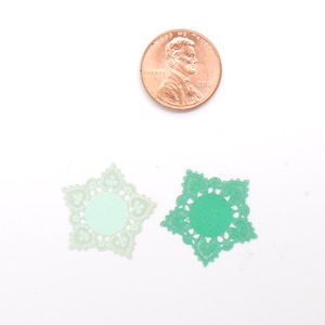 Puede incluir: Dos servilletas de papel verde en forma de estrella. Las servilletas tienen un delicado diseño de encaje y son aproximadamente del tamaño de una moneda de un centavo de euro.